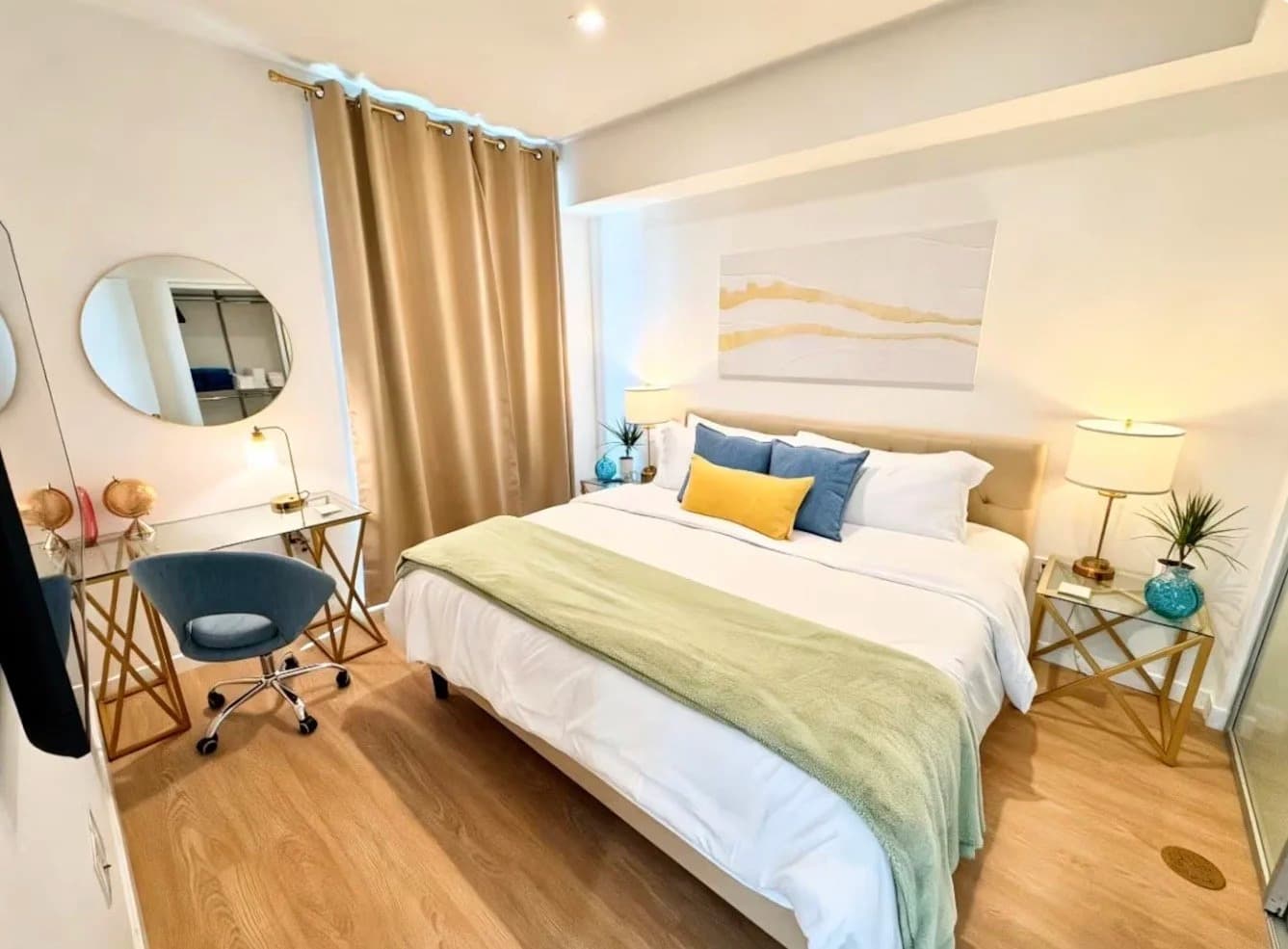 Furnished bedroom with king bed, blackout curtains, gold nightstands and glass desk workspace in a Santa Monica rental
