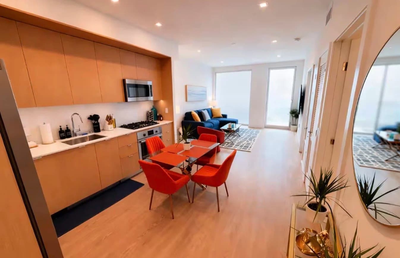 Open-plan living, kitchen and dining area with a navy sofa and balcony doors in a Santa Monica furnished rental