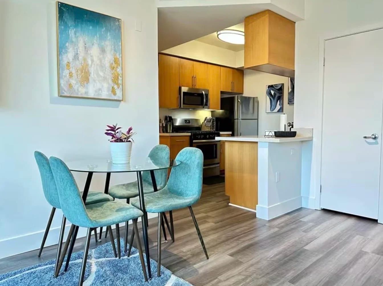 Furnished dining area with glass table, teal chairs and open kitchen in a Santa Monica monthly rental